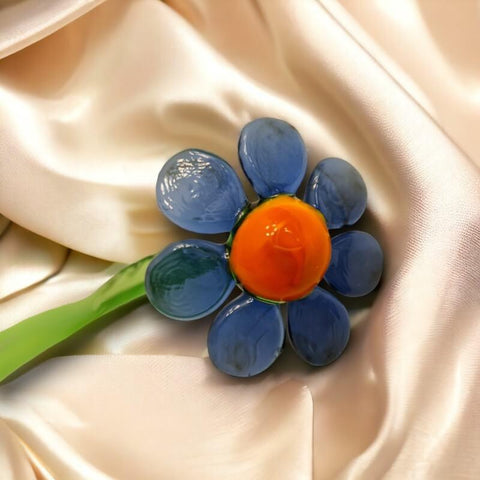 a blue and orange flower brooch sitting on a white satin